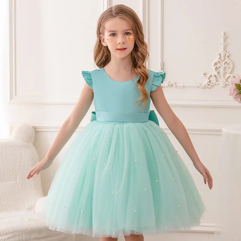 A girl wearing a mint green 'Chantelle-Elise' V-Back Occasion Dress, adorned with tulle and subtle embellishments, perfect for weddings or parties.