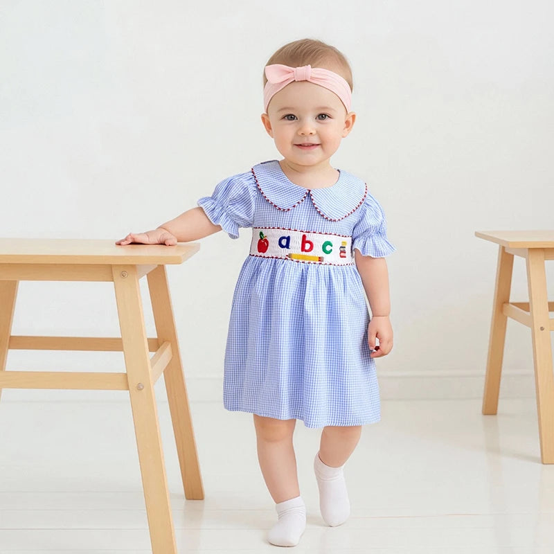 A little girl happily walking with a playful pose in the ABCs Embroidered Girls Dress - Peter Pan Collar, featuring vibrant embroidery and puff sleeves.