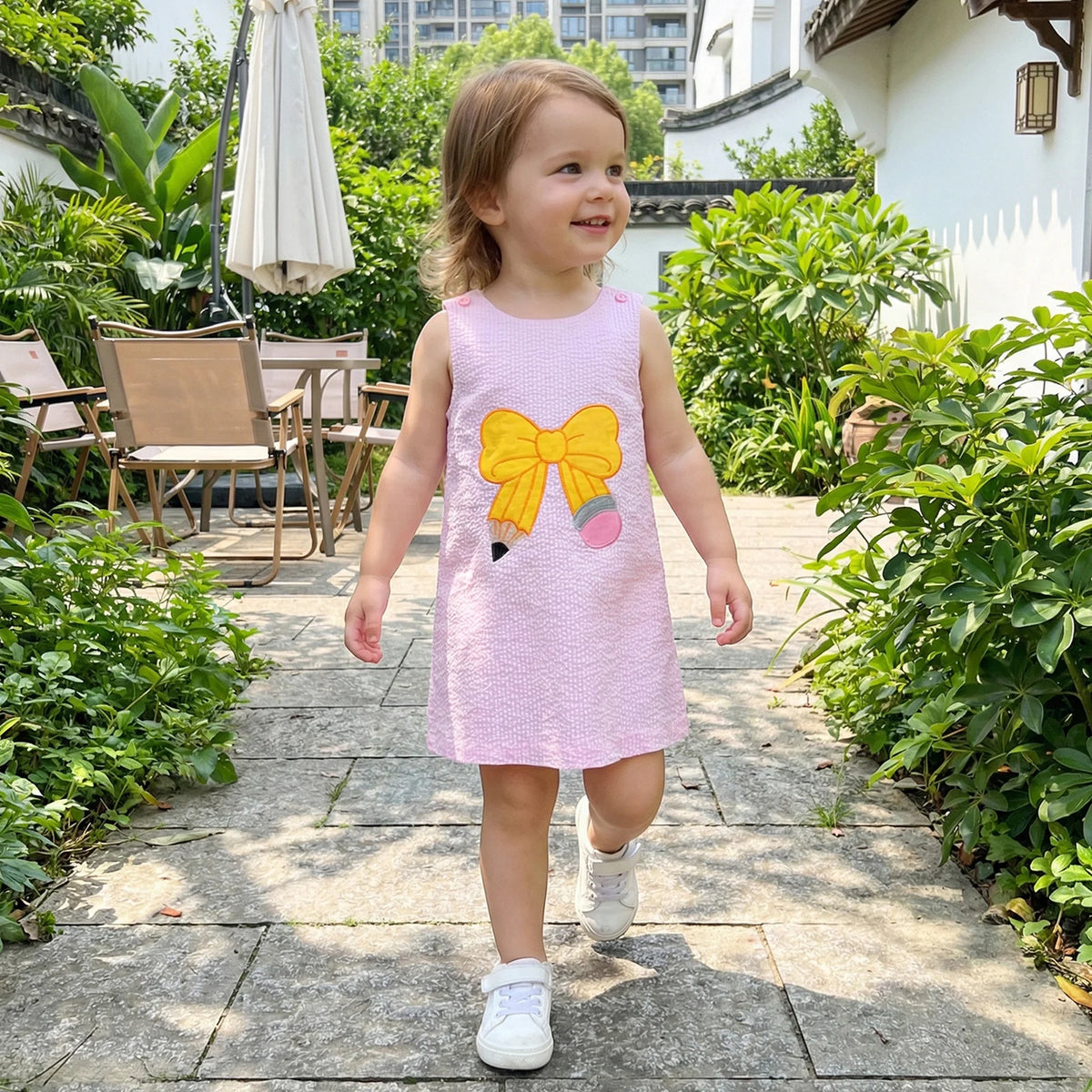 Back to School seersucker sleeveless embroidered dress with yellow bow worn by a smiling girl
