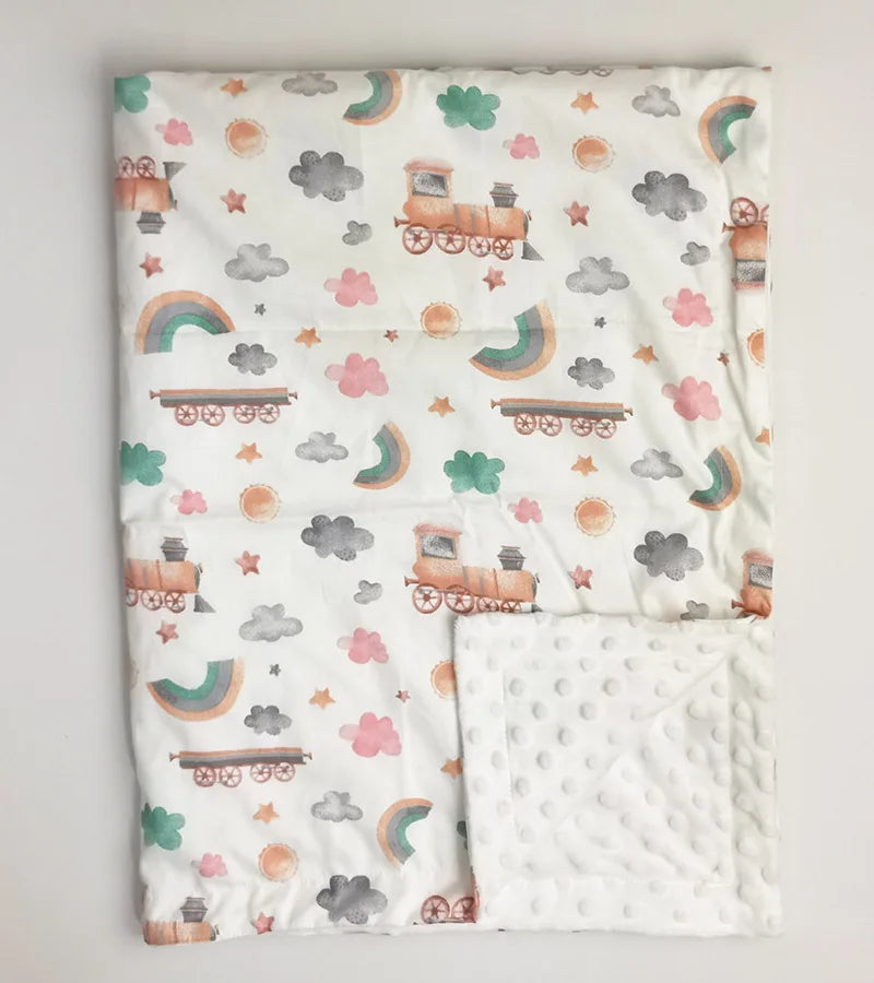 Soft white baby blanket featuring train, rainbow, and cloud print. Shows textured minky dot backing. 100x75cm ultra-soft blanket for toddlers.