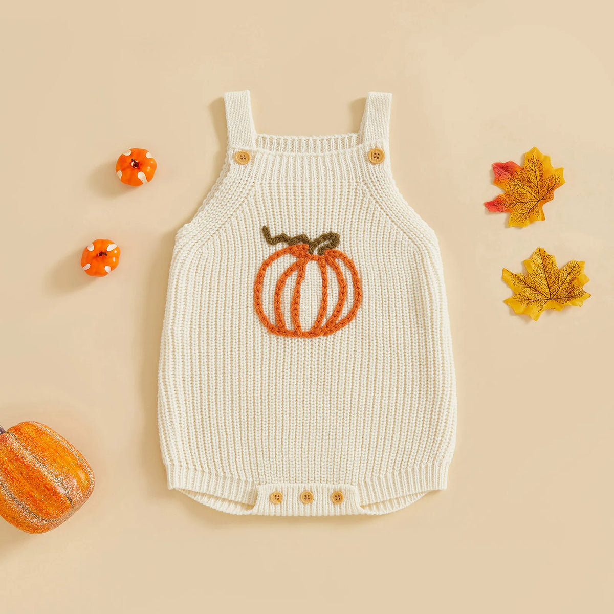 Cream knit romper overalls with embroidered orange pumpkin, styled with mini pumpkins and autumn leaves for babies.