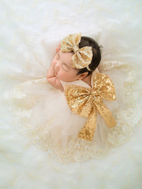 Infant girl in gold sequin oversized bow headband with matching bow dress and lace accents.