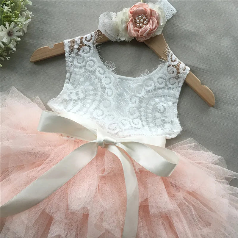 White beaded lace dress for girls with pink tulle skirt, satin belt bow, and matching headband.