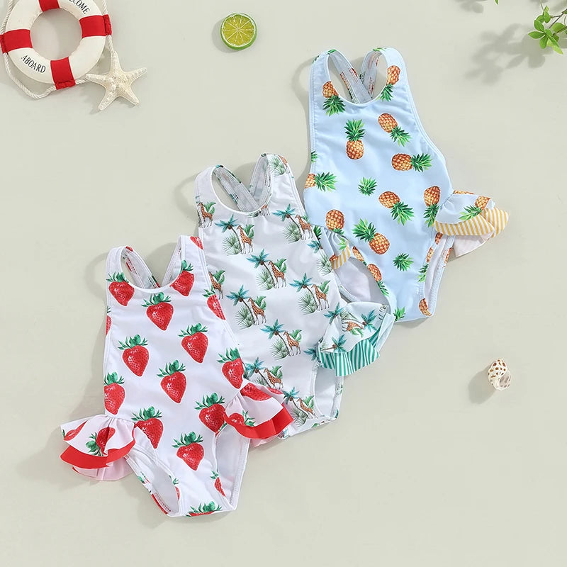 Four toddler girls' one-piece swimsuits with crisscross backs and frills, strawberry, palm-camel, pineapple prints.