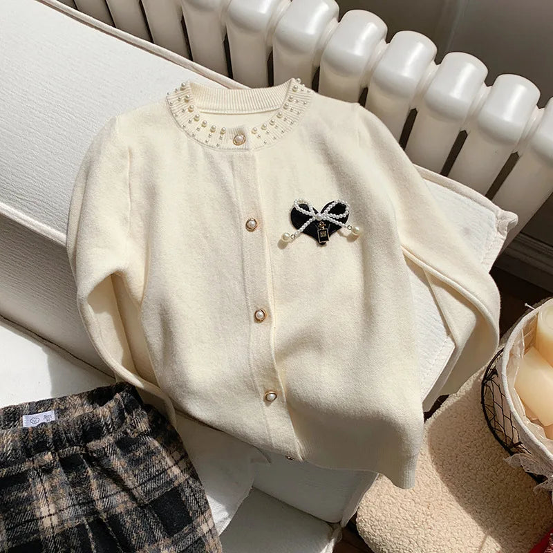 A close-up of the cream Bows and Pearls Little Girls Cardigan showing the faux pearl buttons and bow details, perfect for adding elegance to a girl's outfit.