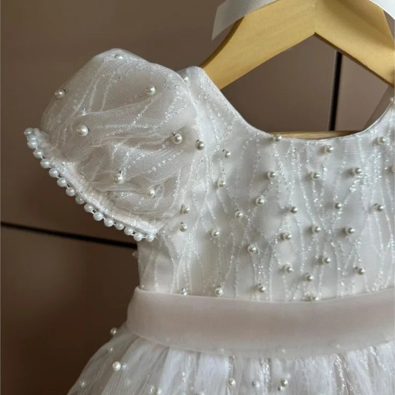 White dress with pearl embellishments on a wooden hanger against a neutral background