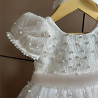 White dress with pearl embellishments on a wooden hanger against a neutral background