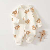 White quilted baby romper with brown teddy bear print, long sleeves, front buttons, and a wooden rattle.