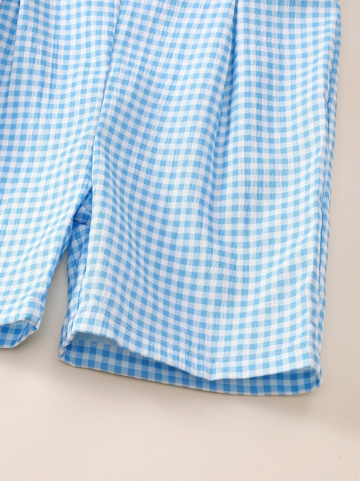 Blue and white gingham fabric detail of a sleeveless baby romper with button closures for infants and toddlers.
