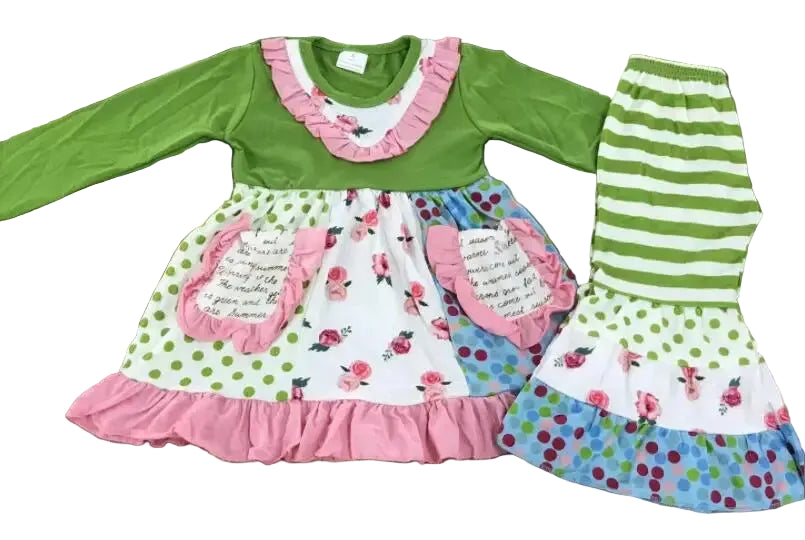 A children's two-piece outfit laid flat on a wooden floor, featuring a green long-sleeve top with pink ruffle trim and a white floral skirt with green polka dots and pink ruffles, paired with matching green-and-white striped leggings.