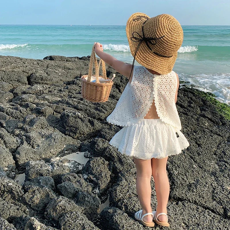Little girl wearing Wentworth white Summer and Lace 2-Piece Skort and Top Set on rocky beach with straw hat.