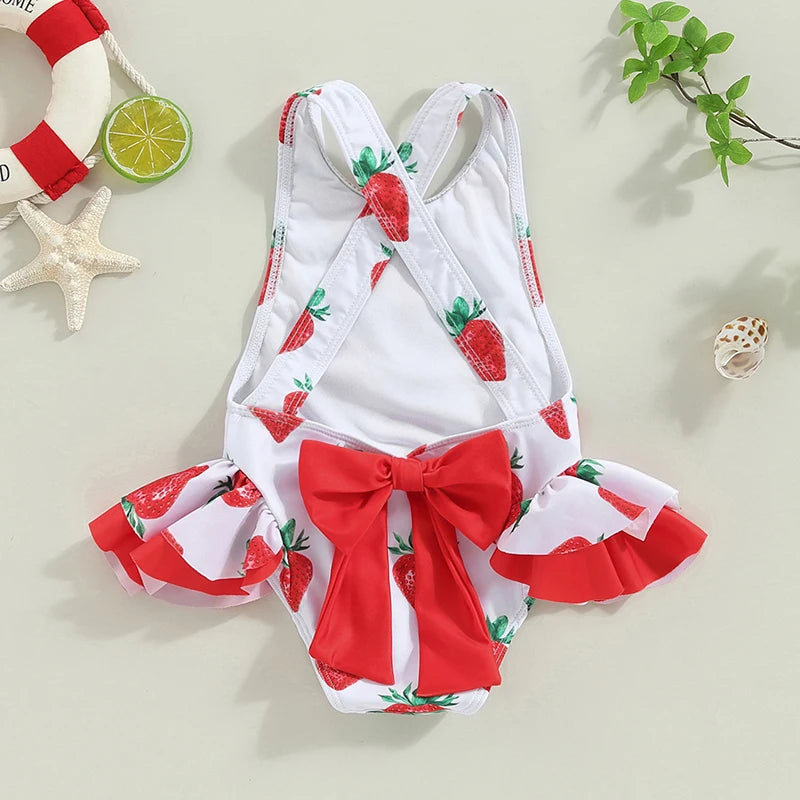 Frilly strawberry-print toddler one-piece swimsuit with cross-back straps and a bold red bow.