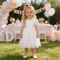 Toddler girl in knee-length white lace baptism dress with pink waist sash, embroidered short sleeves, round neckline