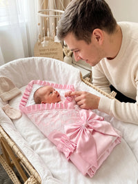 Palm Beach Pink satin lace baby receiving blanket with ruffle and large bow in a bassinet beside a father