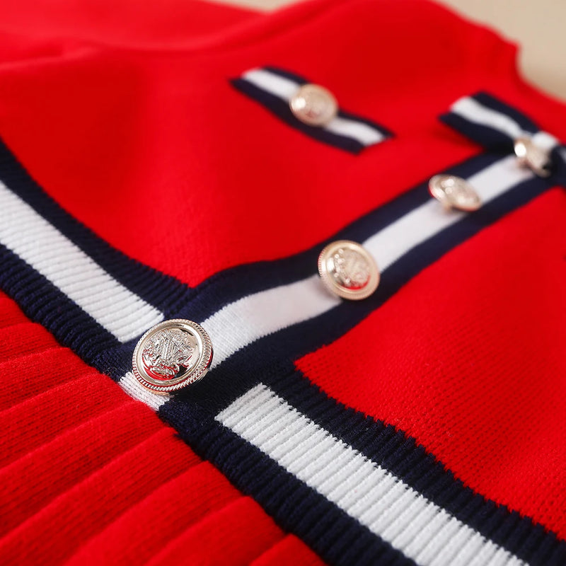 Close-up of the Preppy Darla Knit Dress Long Sleeves showcasing elegant gold buttons and playful bow accents against a red background.