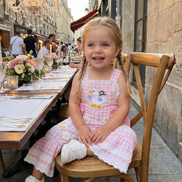 Young girl in a pink dress sitting at an outdoor dining table with a city street background.