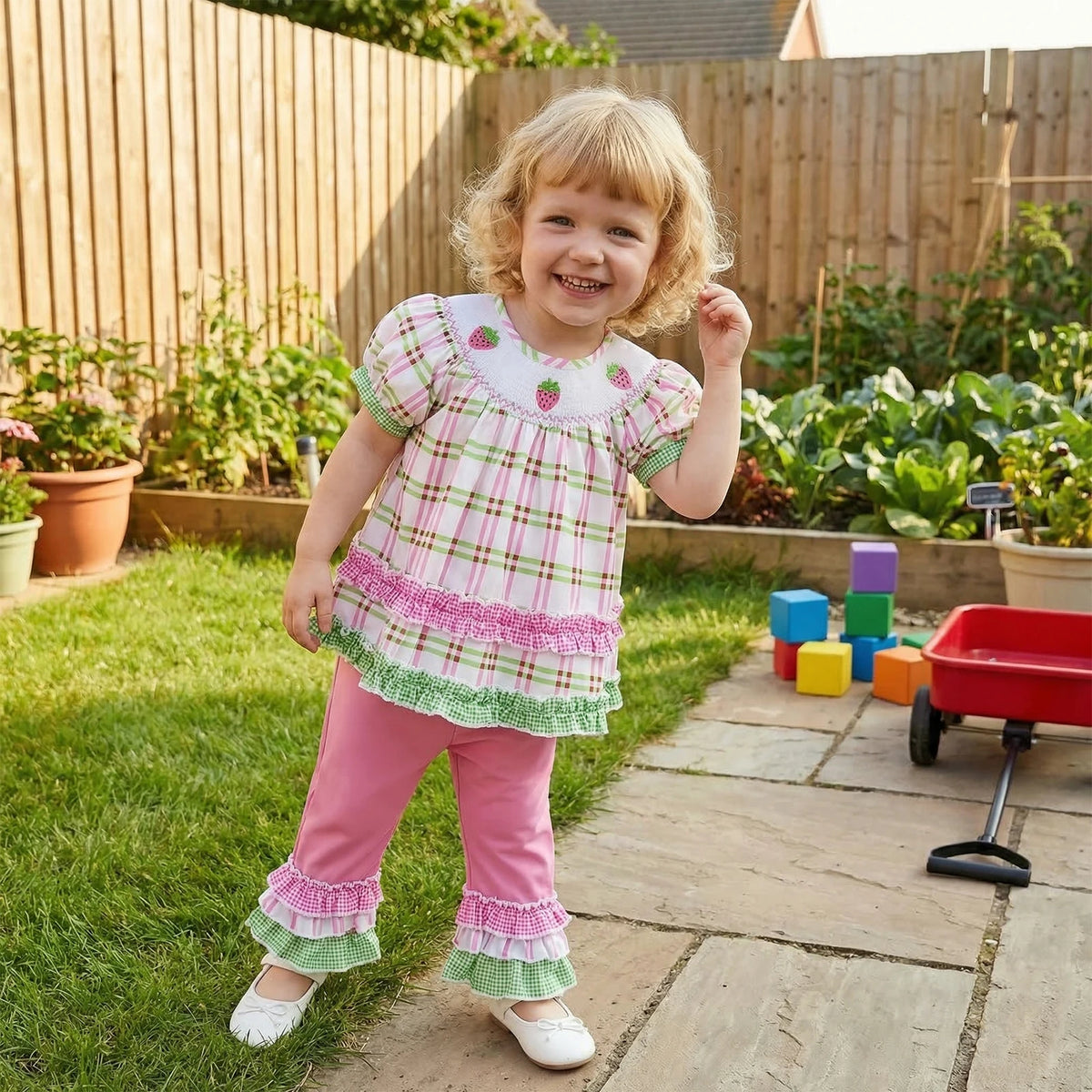 Girl wearing frilly boho plaid two-piece outfit with puff sleeves and ruffles outdoors in a garden.