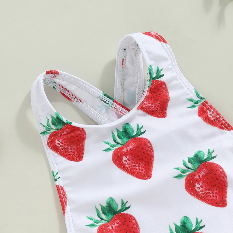 White one-piece toddler swimsuit with red strawberry print, crisscross back straps and frilly accents.
