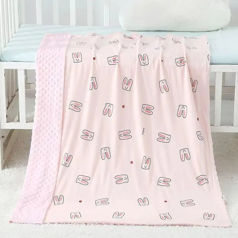 Soft pink baby minky blanket featuring cute bunny illustrations and textured border, draped over a white crib for a cozy nursery.