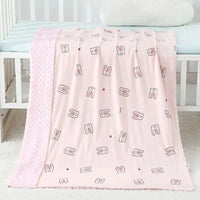 Soft pink baby minky blanket featuring cute bunny illustrations and textured border, draped over a white crib for a cozy nursery.