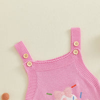 Pink knitted romper overalls with shoulder straps, cream buttons, and cupcake embroidery for a first birthday outfit