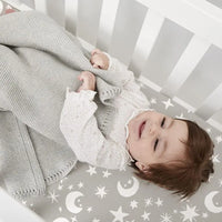 Baby on a gray star-and-moon microfiber crib sheet; part of a 4-pack extra soft crib sheets set.