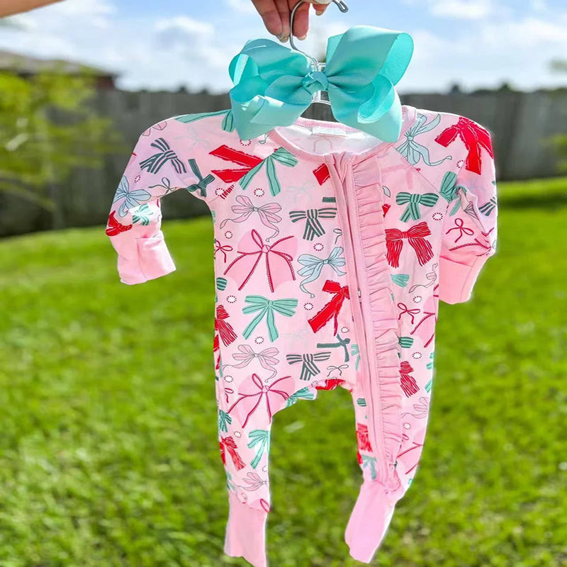 The delightful ‘Bow-licious’ Ruffle Baby Romper in Palm Beach Pink hangs gracefully, displaying its fun bow designs. This cozy ruffle baby romper is perfect for any occasion, showcasing style and comfort for young girls.