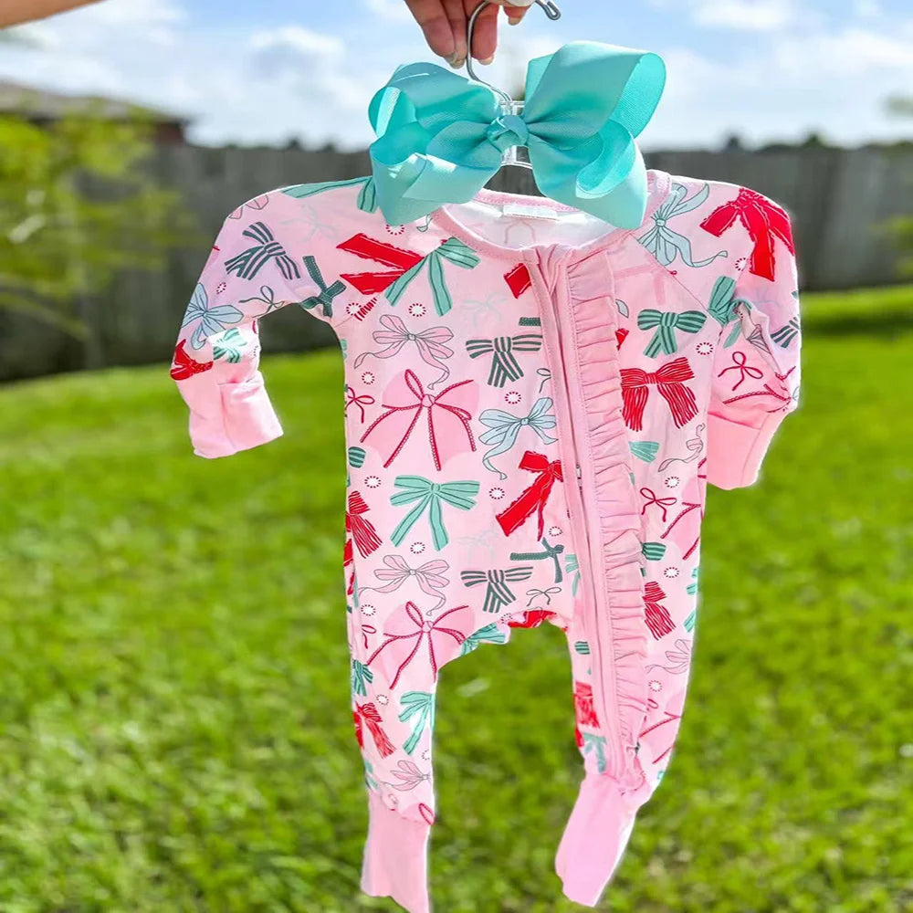 A charming ‘Bow-licious’ Ruffle Baby Romper in Palm Beach Pink, featuring a vibrant bow pattern and designed for comfort. Perfect for little girls, this ruffle baby romper is showcased against a sunny outdoor backdrop.