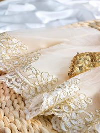Ivory infant gown fabric with gold sequined bow and floral embroidered lace edges.