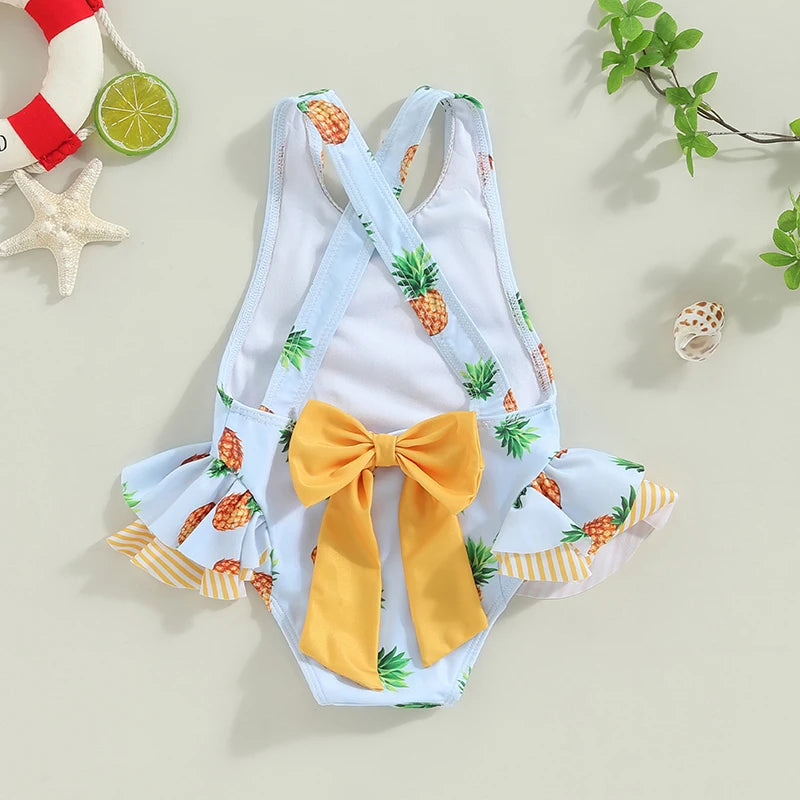 Pineapple-print light-blue toddler girls' 1-piece swimsuit with cross-back straps and yellow bow, frilled sides.
