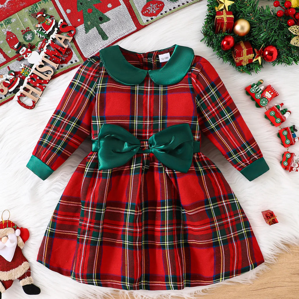 Louisa Girls Red Plaid Bow Dress displayed on a festive background with Christmas decorations, showcasing its charming plaid pattern, spruce satin bow, and Peter Pan collar.