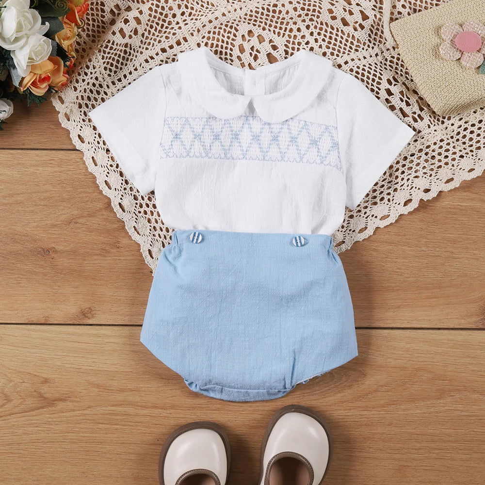 The "Hamilton" Boys Short-Sleeved Smocked Shorts Set featuring a white short-sleeve shirt with a classic collar and elegant Boca blue shorts, perfect for stylish toddlers.