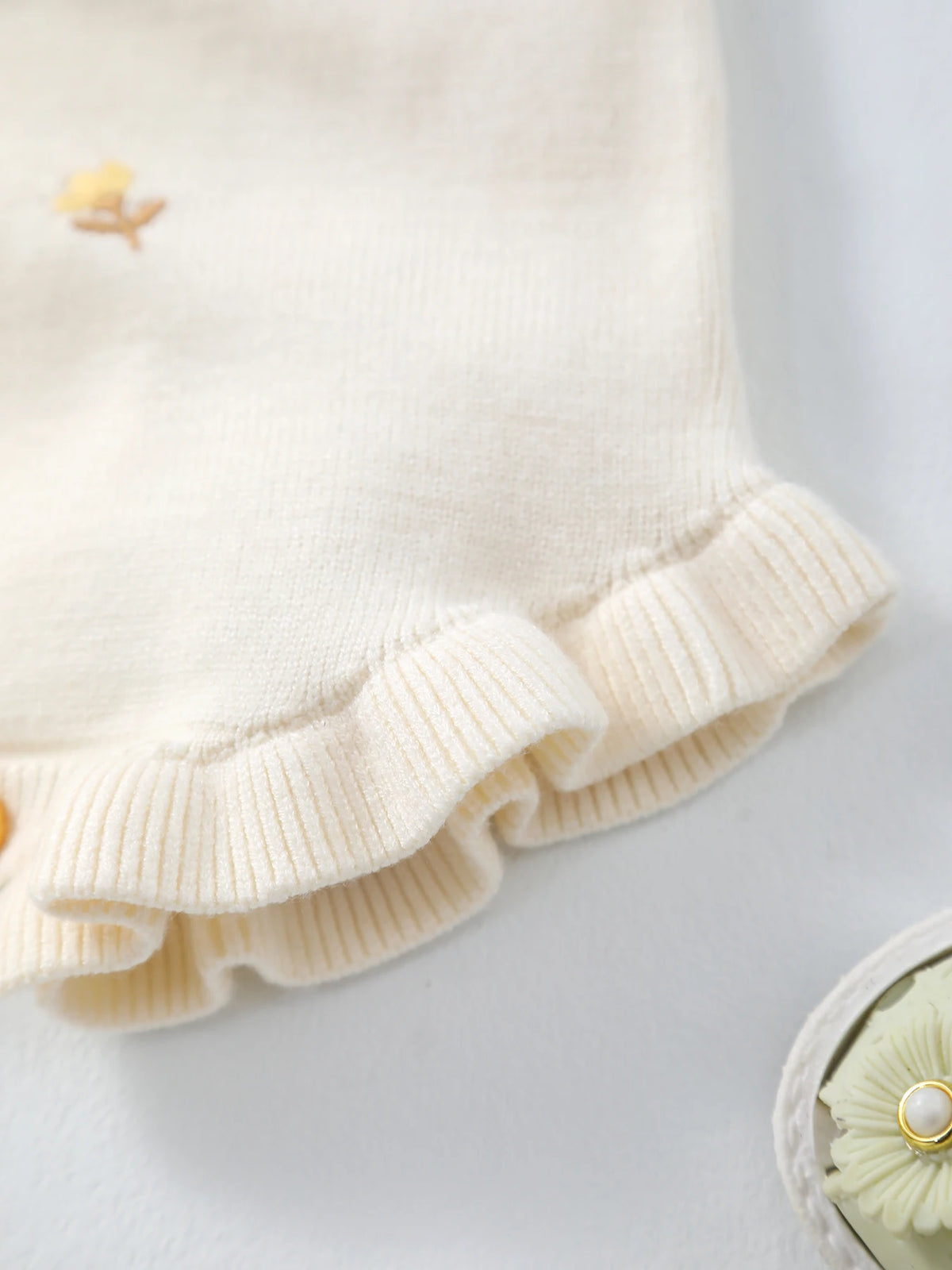 Cream knit romper with frilly cuffs and crocheted yellow floral detail; for babies to 18 months.