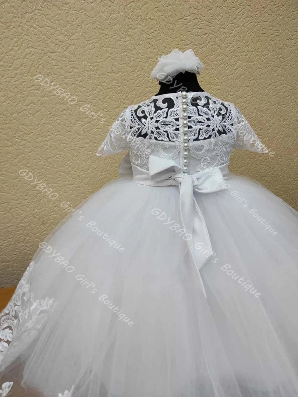 White lace flower girl dress back view featuring faux pearl buttons, large ribbon bow, and tiered tulle skirt for weddings.