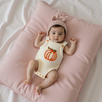 Baby wearing cream knit pumpkin patch romper overalls with matching pink bow hat on soft pink pillow.