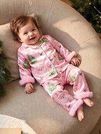 Baby girl wearing pink satin Christmas pajama set with Santa and tree print and fuzzy cuffs.