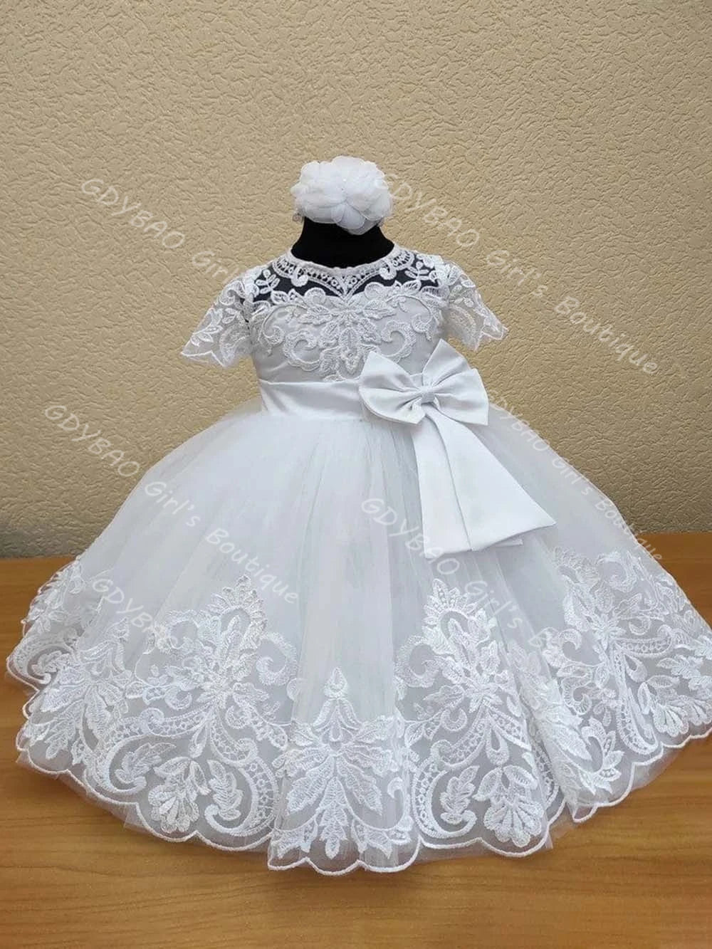White lace flower girl dress with tiered tulle skirt, intricate appliques, and large back bow for weddings or special occasions.