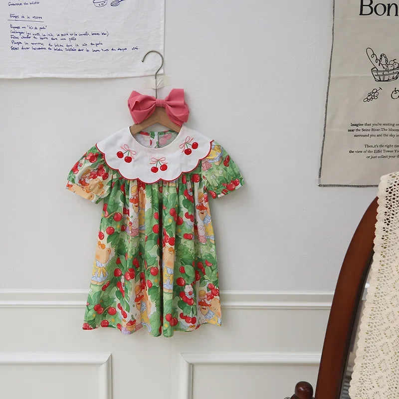 A Very Cherry Day Embroidered Dress showcased on a wall, emphasizing the cute cherry print dress and its delightful embroidered details.