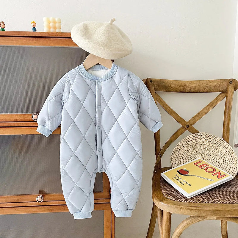 Charming blue baby quilted romper on a wooden chair, styled with a beret, showcasing its cozy design for little ones.