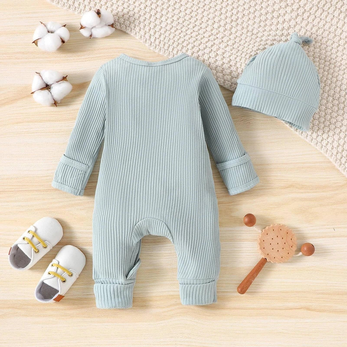 Light blue ribbed romper and matching hat for babies displayed flat with white baby shoes and wooden toy