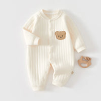 Cream quilted baby romper with long sleeves, front buttons, and a cute bear patch, shown with a wooden teether.