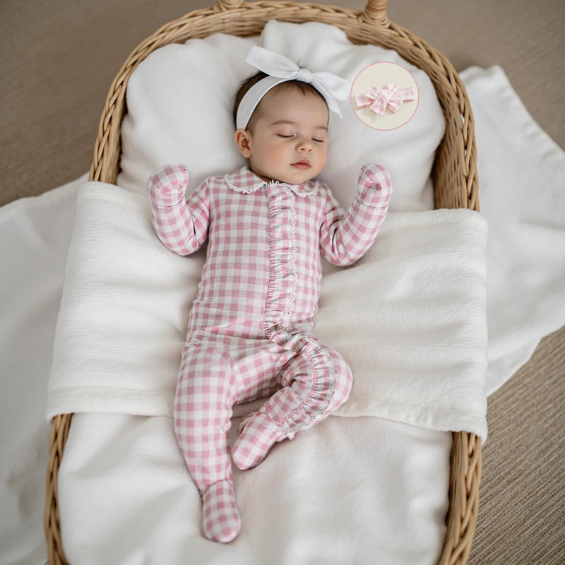 Adorable baby girl sleeping in a cozy Checks and Frills Footie Set in Poinciana pink, complete with a matching headbow.