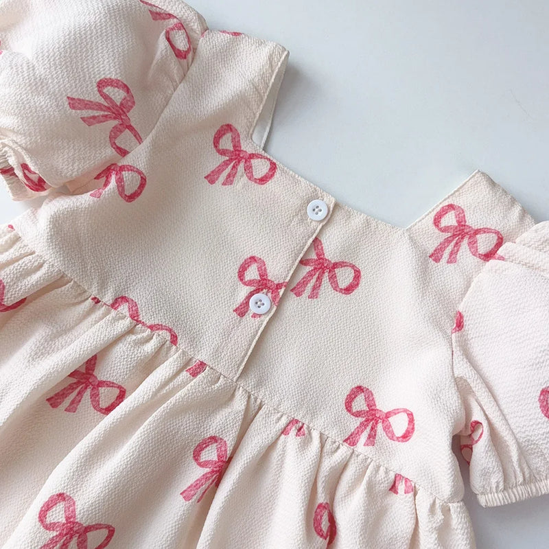 Close-up view of the 'Sweet Little Bows' Party Dress featuring a soft pastel pink fabric with adorable printed bows. Showcasing the square neckline and playful puff sleeves, this dress is designed for girls aged 3 to 7, perfect for twirling at parties.
