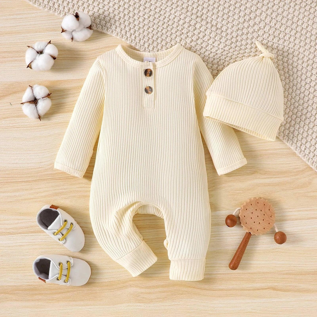 cream ribbed romper for babies with matching hat and white baby shoes next to wooden toy