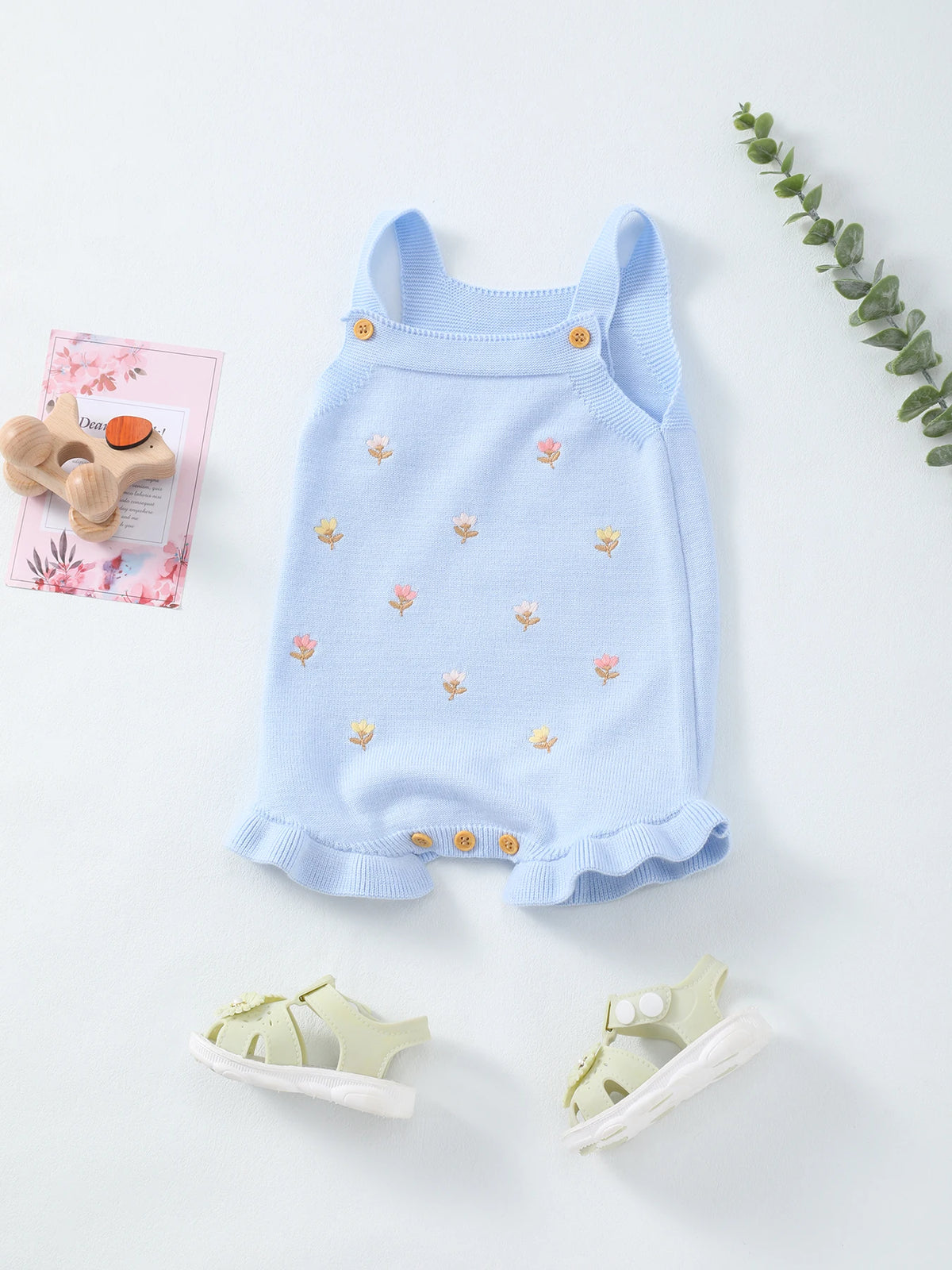 Light blue knit baby romper with tiny floral embroidery, frilled hem, sleeveless straps, and buttoned leg openings.