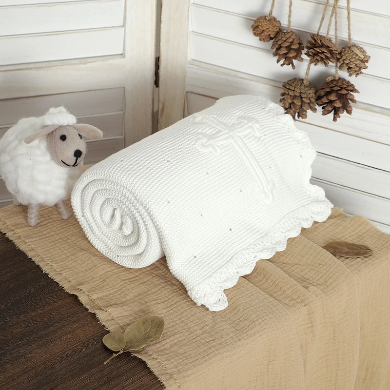 White cotton baptism blanket with crocheted cross, 100 x 80 cm, soft knit with lace edge, rolled beside a plush sheep.