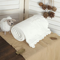 White cotton baptism blanket with crocheted cross, 100 x 80 cm, soft knit with lace edge, rolled beside a plush sheep.