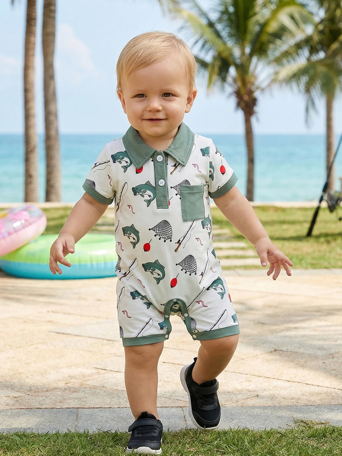 Baby boy in short-sleeve polo-style romper with fishing-themed print, green collar and pocket at the beach.