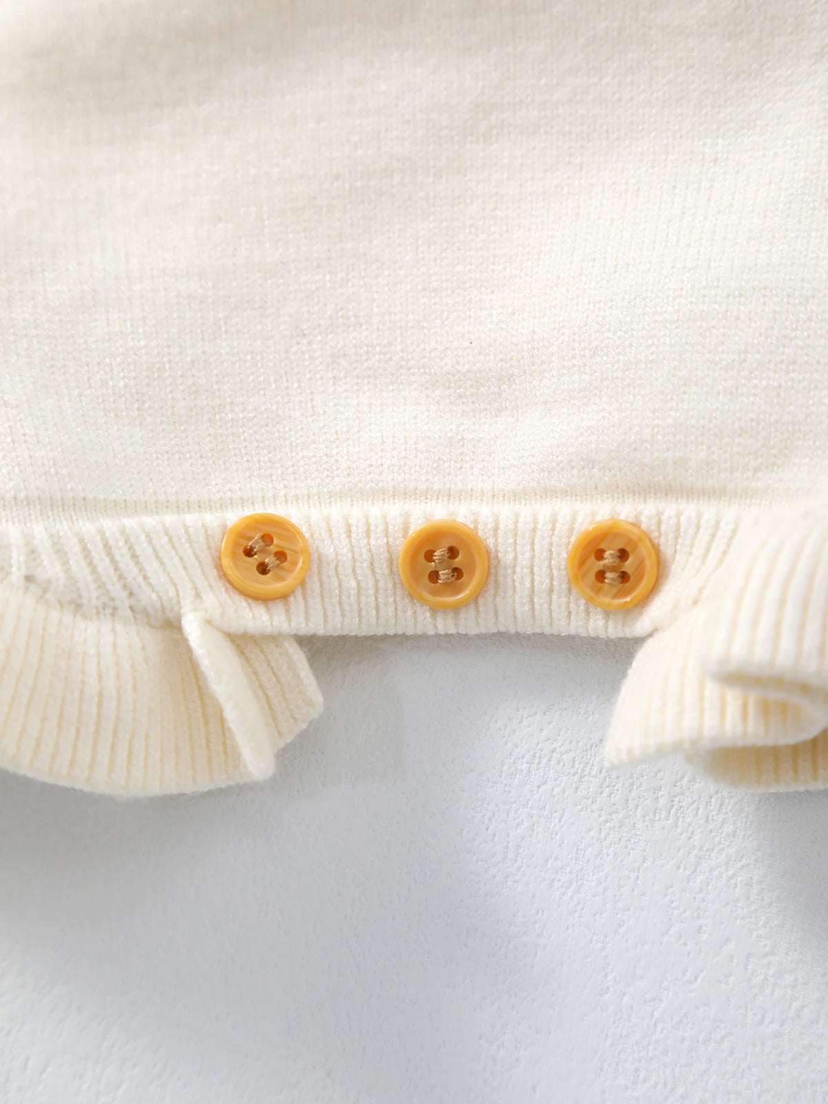 Cream knit baby cardigan with ribbed trim and three peach buttons.