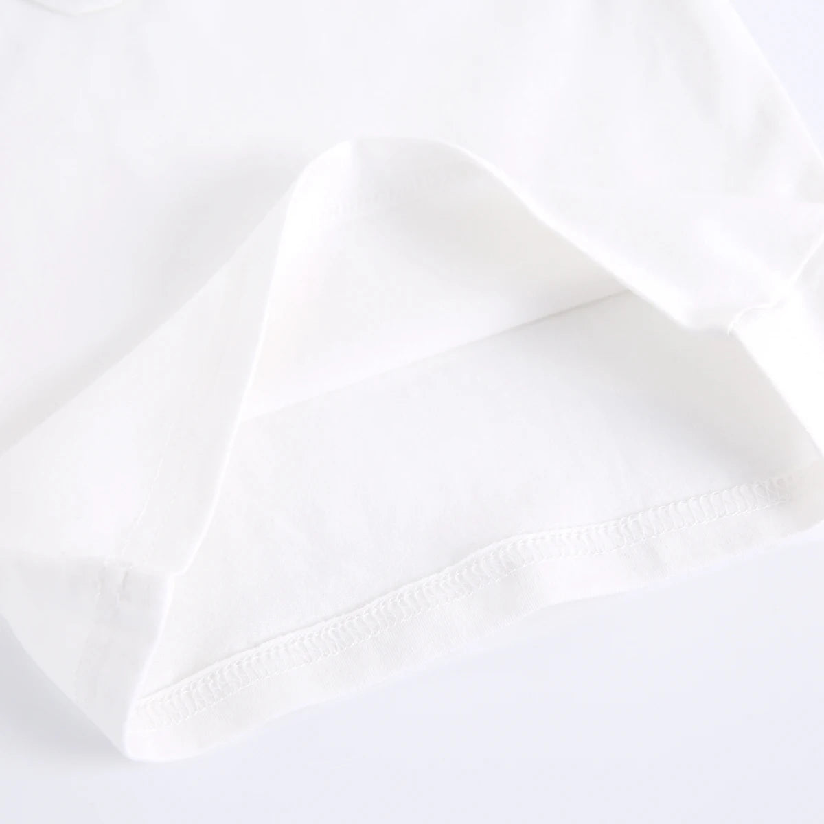 A close-up of a plain white cotton fabric, showing a folded corner and a neat hem with fine stitching.